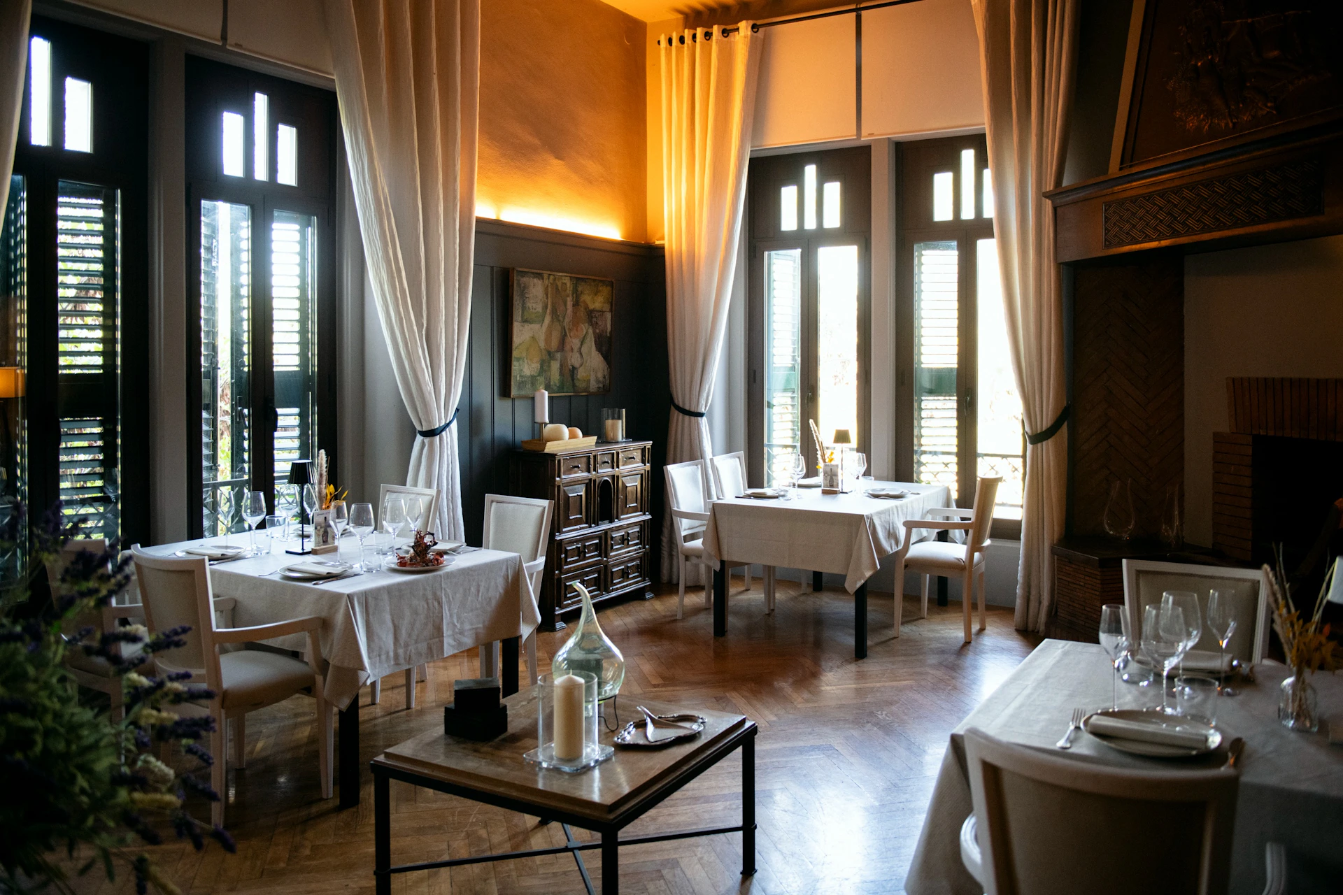 A cozy restaurant interior with elegant white tablecloths, wooden furniture, and soft natural light through tall windows.