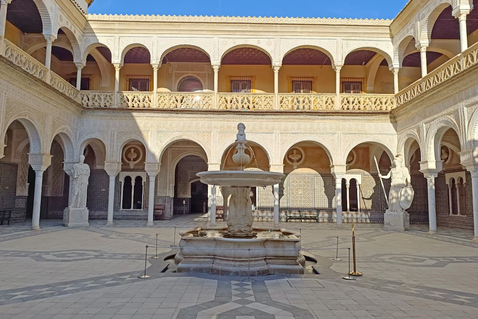 An ornate courtyard featuring arches, a central fountain with a statue, and two floors of decorative architecture.