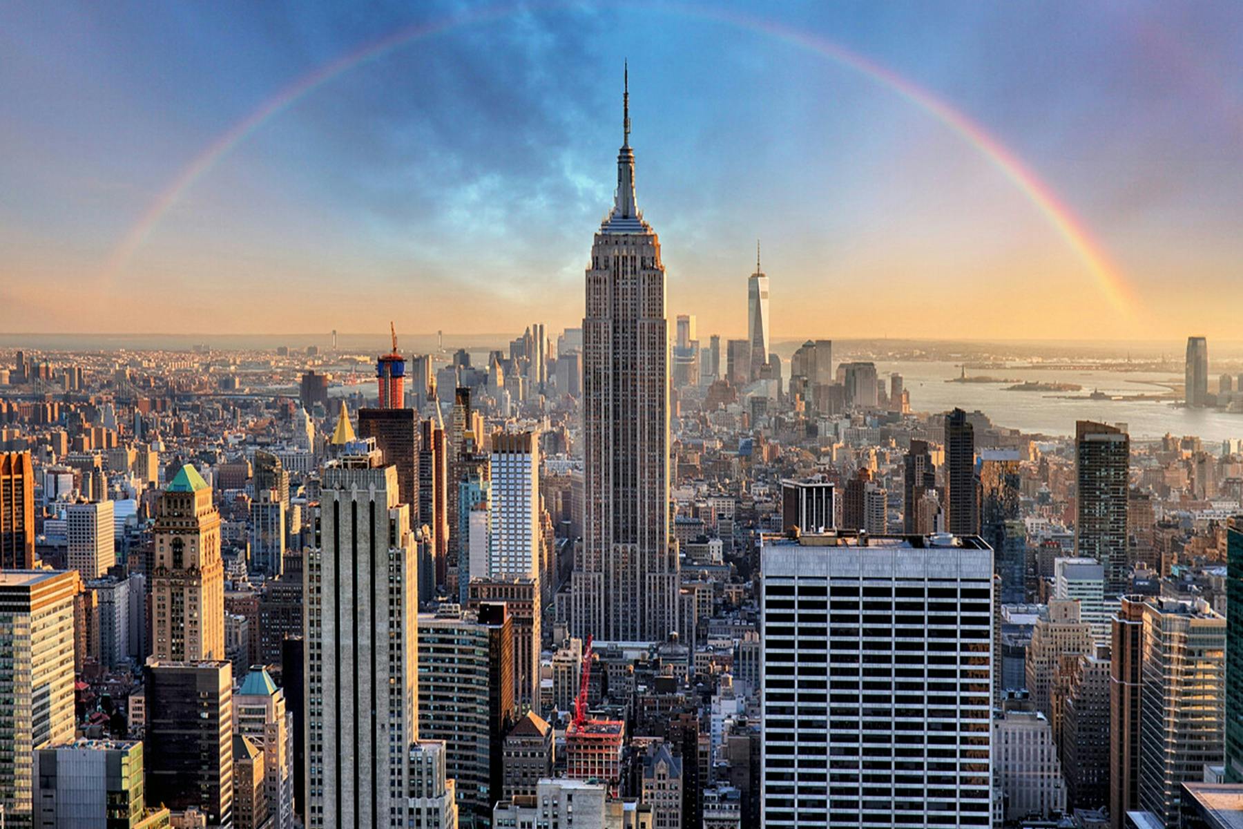 Utsikt över en stadssilhuett med Empire State Building i centrum, andra skyskrapor runtomkring och en delvis regnbåge som böjs över.