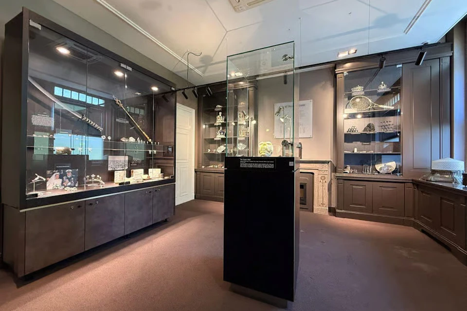 A museum display room featuring glass cases with jewelry and artifacts, including crowns and decorative items.