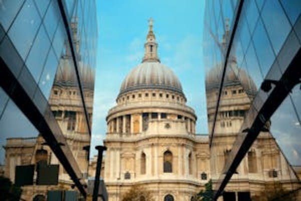 Une statue d'un personnage assis tenant un sceptre, placée dans une fontaine devant un bâtiment historique en briques avec des pelouses entretenues.
