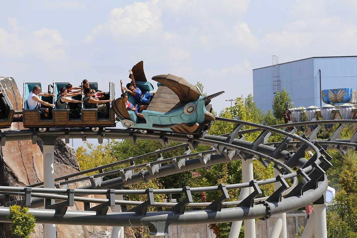 People riding a detailed, dragon-themed rollercoaster on a sunny day with trees and a building in the background.