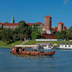 En träbåt med människor på en flod, med ett stort, historiskt slott och gröna träd i bakgrunden under en klarblå himmel.