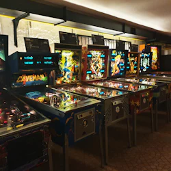 En rad vintage-flipperspel med upplysta skärmar och färgglada konstverk i en arkadmiljö.