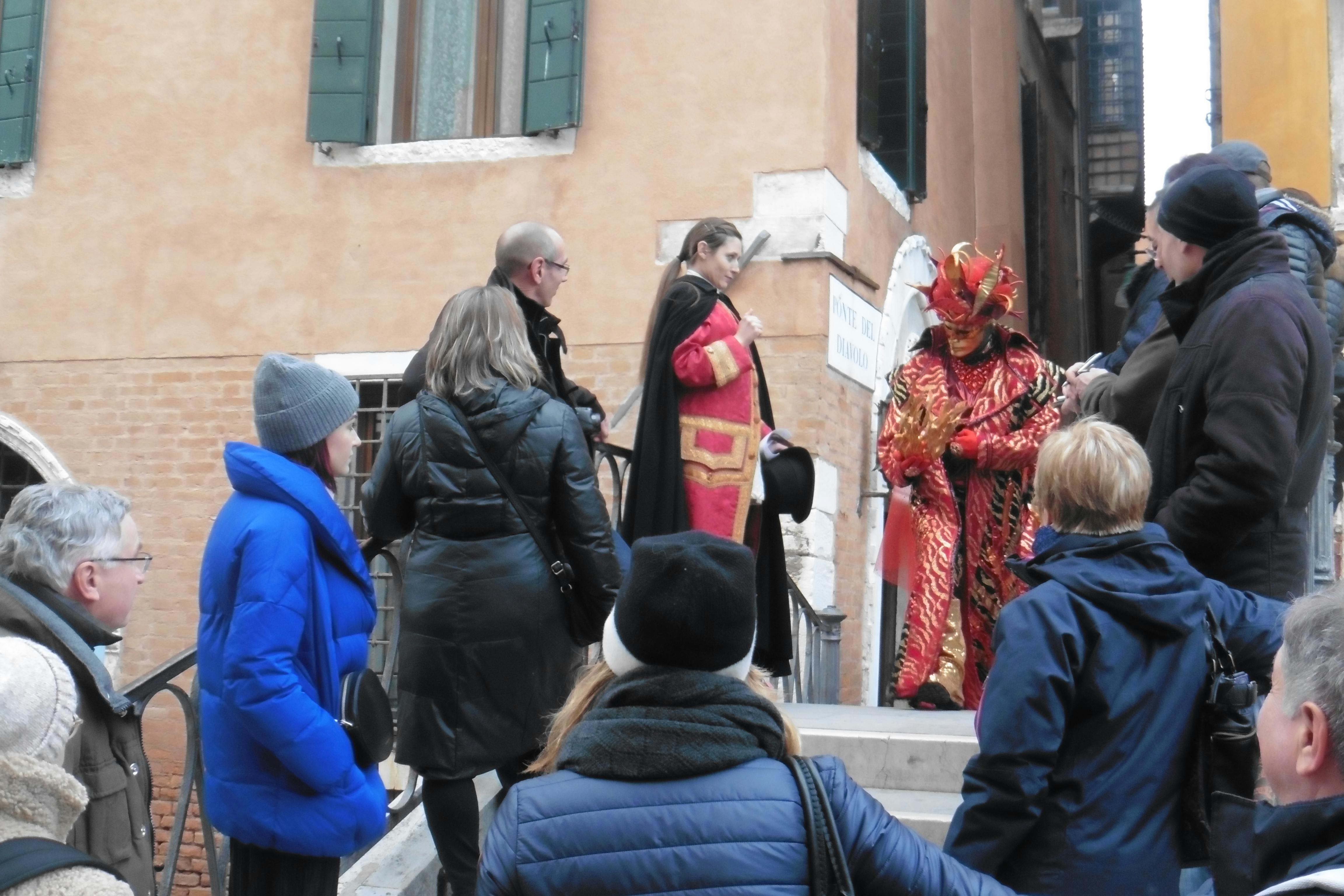 冬の衣装を着た人々は、精巧な衣装を着た2人の人物の周りに集まります。1人は鮮やかな赤と金の服を着て、屋外の階段にいます。