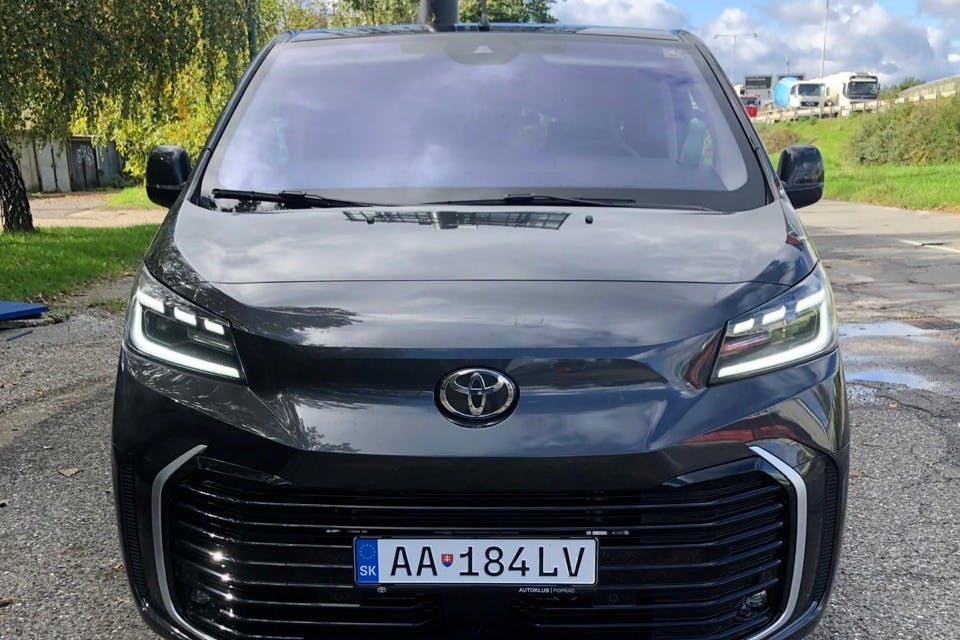 一辆黑色丰田汽车，欧洲车牌号为“AA 184 LV” ，停在户外，后面有树木和蓝天。