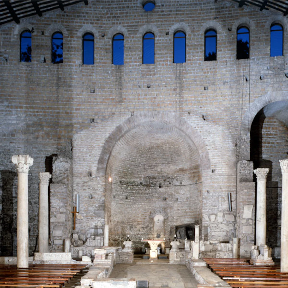 Historic stone interior with high arched ceiling, tall columns, and rows of benches leading to an altar.