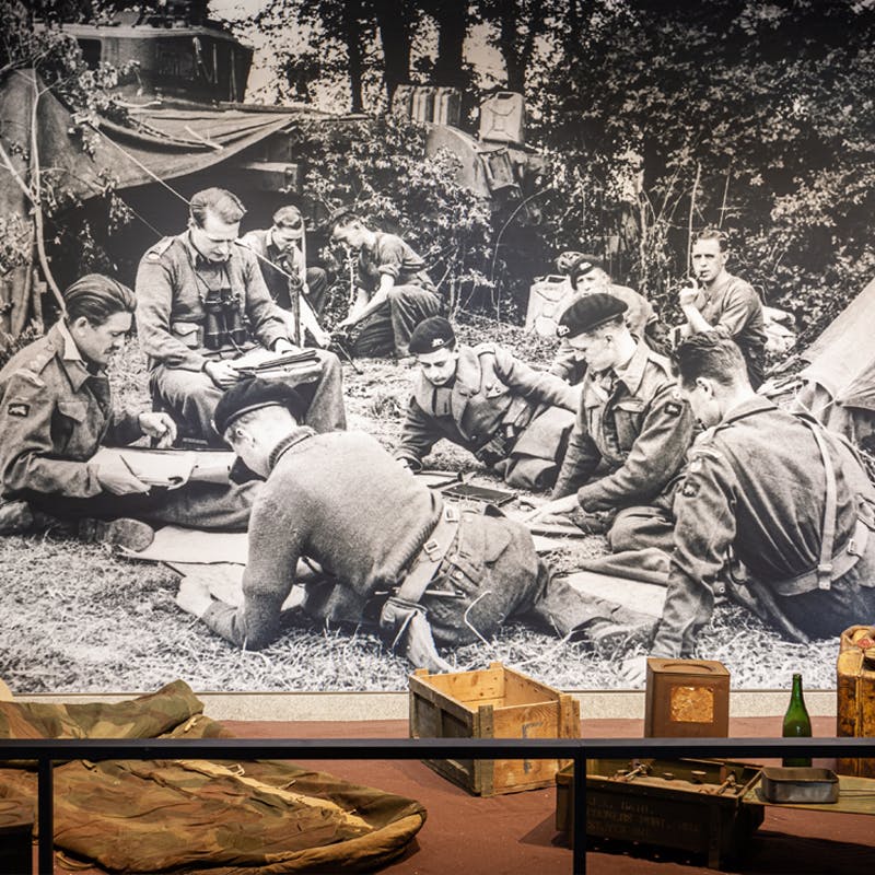 Una foto in bianco e nero di soldati in un campeggio, con varie attrezzature e casse in primo piano.