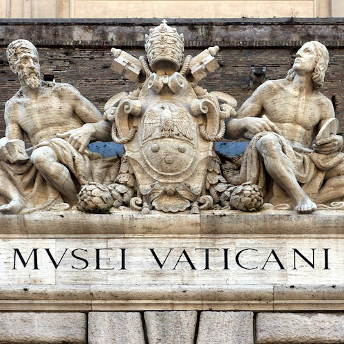 Le statue in pietra di due figure sedute affiancano lo stemma del Vaticano sopra un ingresso con il testo