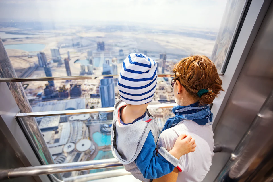 A person holding a child looks out at a cityscape from a high observation deck.