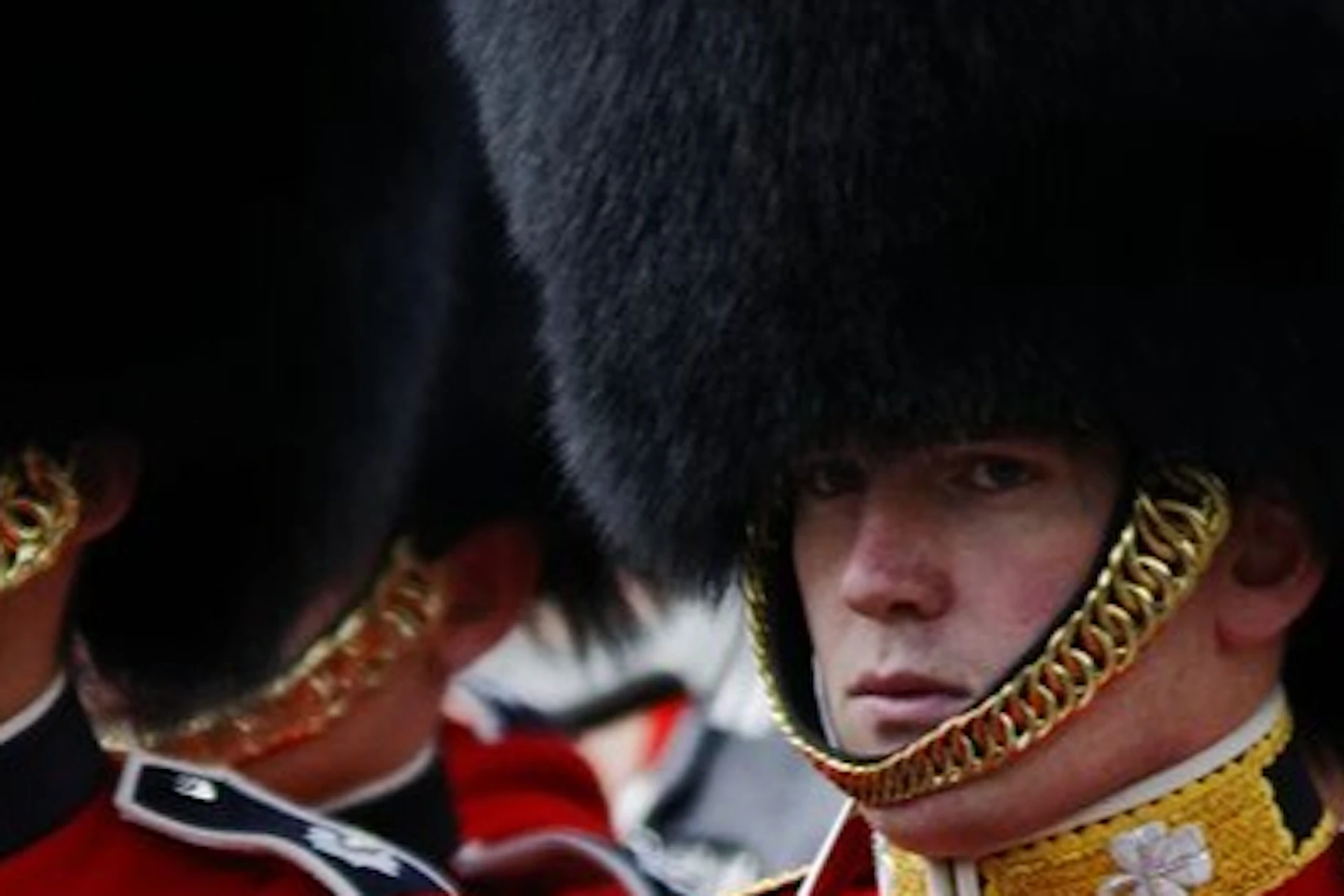 Guards in red uniforms and black fur hats marching in formation, some holding rifles and others wearing gloves.