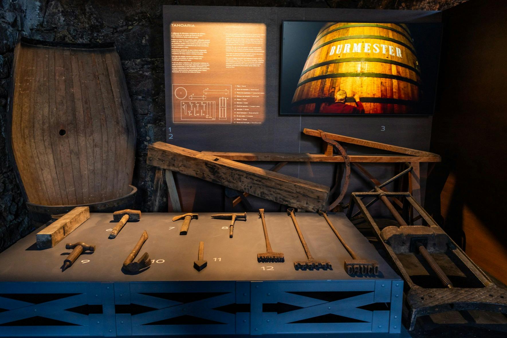 Exposition d'outils de fabrication de tonneaux, de tonneaux en bois et de panneaux d'information dans le cadre d'un musée historique.