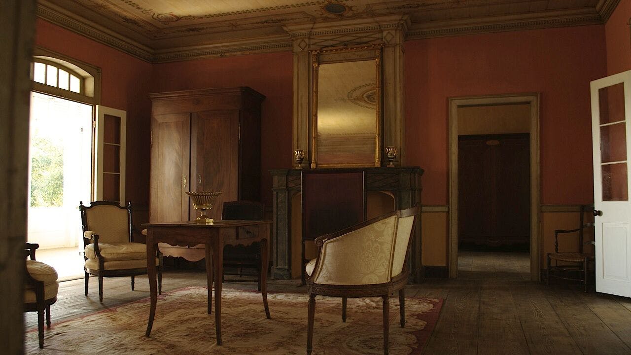 Δωμάτιο vintage με ξύλινο τραπέζι, σκαλιστή καρέκλα, ντουλάπι, ψηλό καθρέφτη πάνω από το τζάκι και περίτεχνες λεπτομέρειες οροφής.