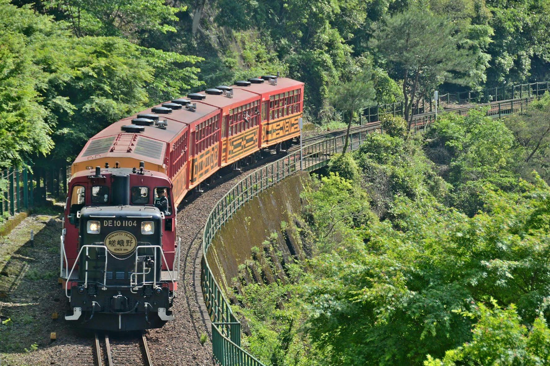 Un train orange et bordeaux circule sur une voie courbe à travers une forêt verdoyante.