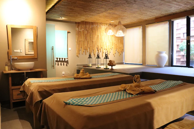 A serene spa room featuring two massage tables with folded towels, bamboo decor, lanterns, and warm lighting.
