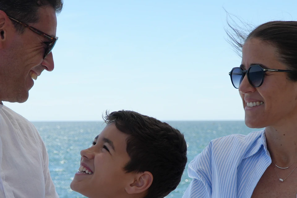 A family of three enjoys drinks and snacks on a boat with a bright blue ocean and clear sky in the background.