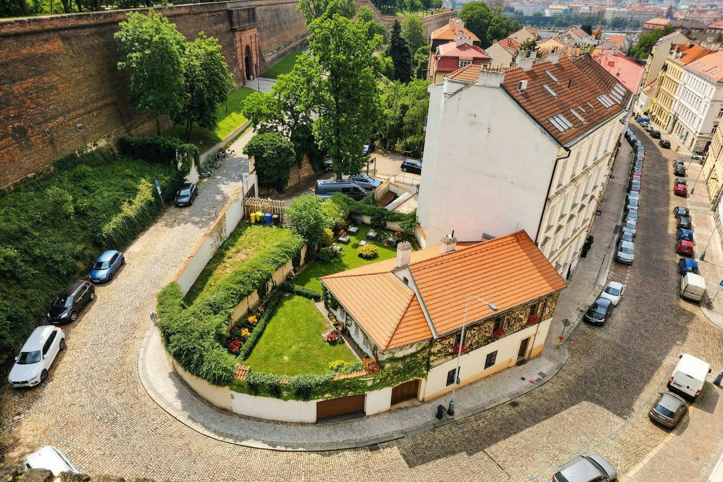 A small house with a red-tiled roof, surrounded by a well-kept garden and a white wall, located in a residential area.