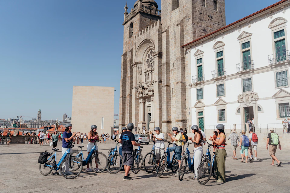 A group of people with helmets standing next to bicycles in a historic plaza with a large stone cathedral in the background.