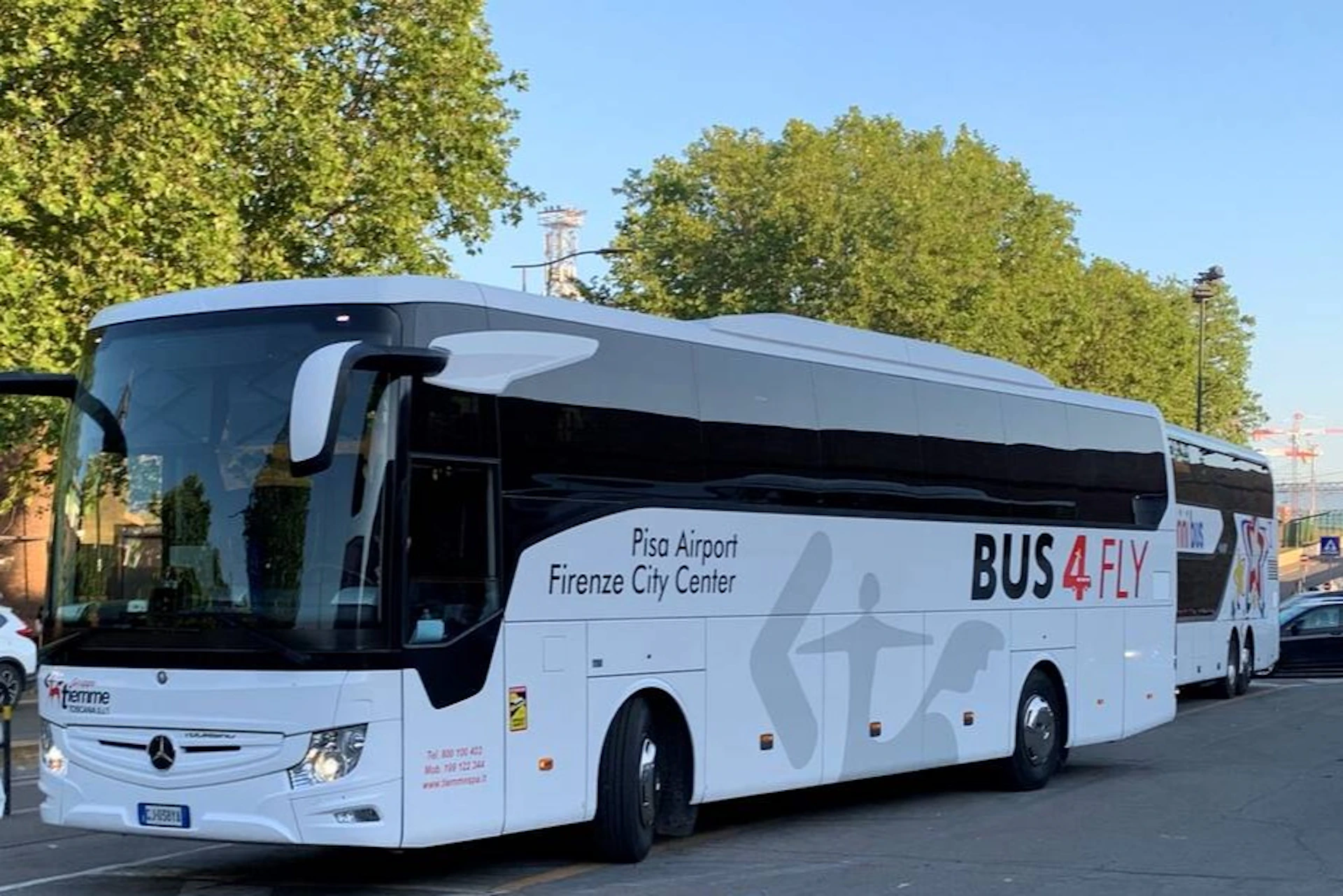 A bus labeled "Pisa Airport Firenze City Center - BUS 4 F" is parked on a road, with green trees in the background.
