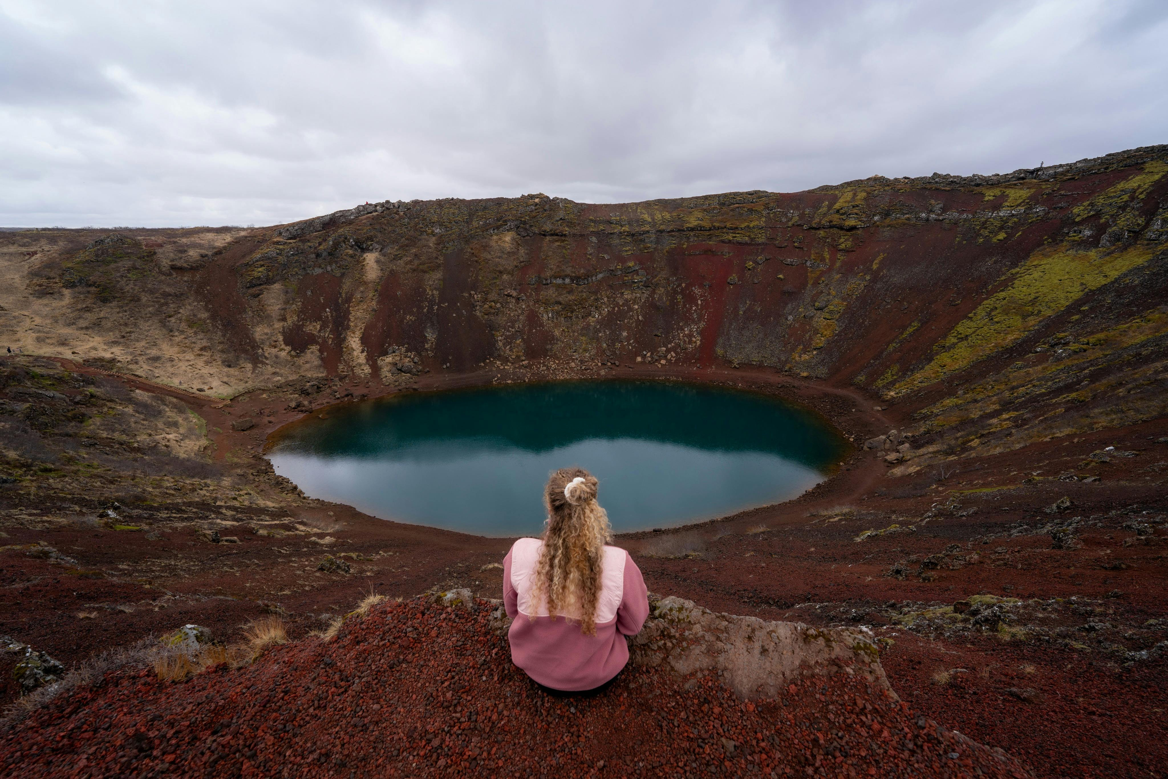 秋天，一位女士坐在那里俯瞰火山口。 红色岩石和绿色苔藓
