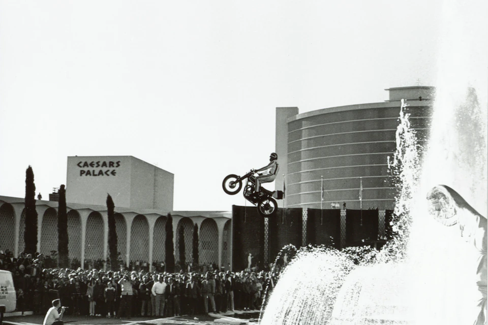 A motorcyclist jumps a fountain at Caesars Palace, with a crowd watching and buildings in the background.