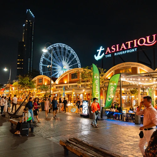 Nächtliche Szene im Asiatique The Riverfront, belebt von Menschen, hellen Lichtern, Geschäften, Restaurants und einem Riesenrad im Hintergrund.