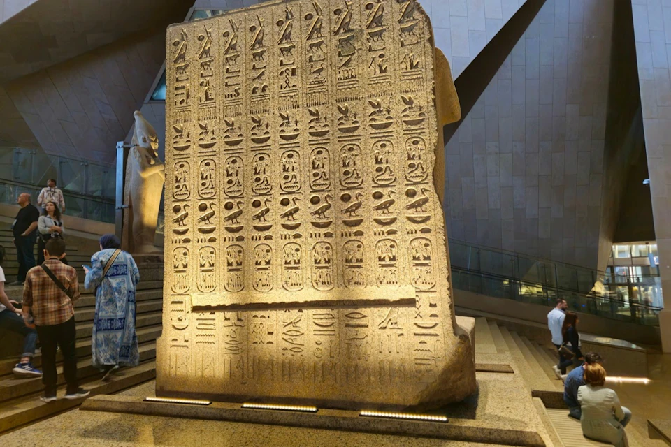 A large ancient stone tablet inscribed with Egyptian hieroglyphs, displayed in a modern museum setting.