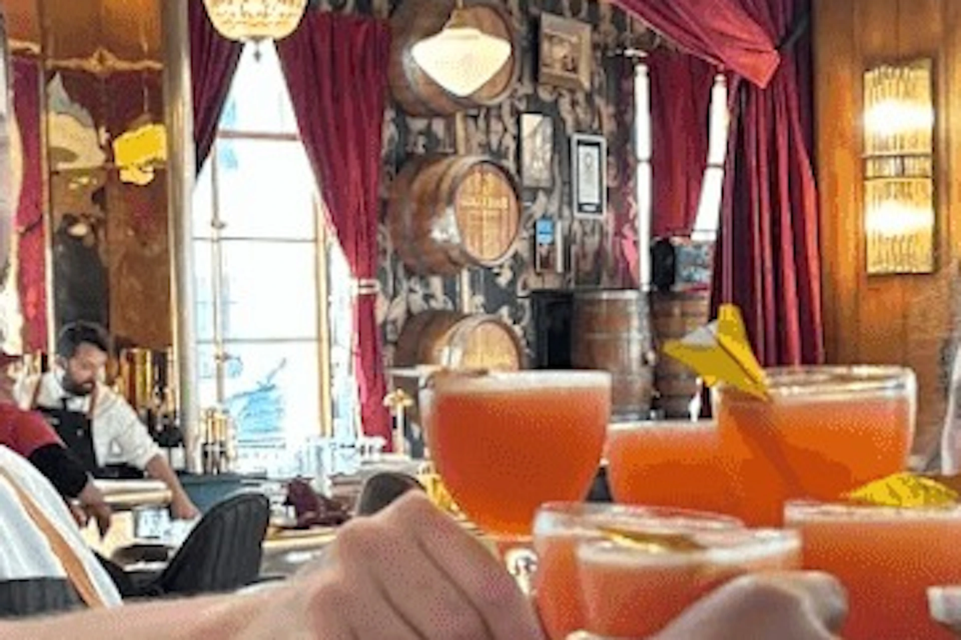 A group of people clinking orange cocktails in a warmly lit restaurant with decorative curtains and wooden furnishings.