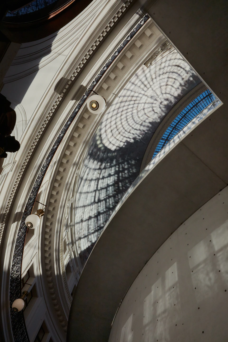 Sunlight creates intricate shadow patterns on a curved, ornate ceiling with a large, arched window.