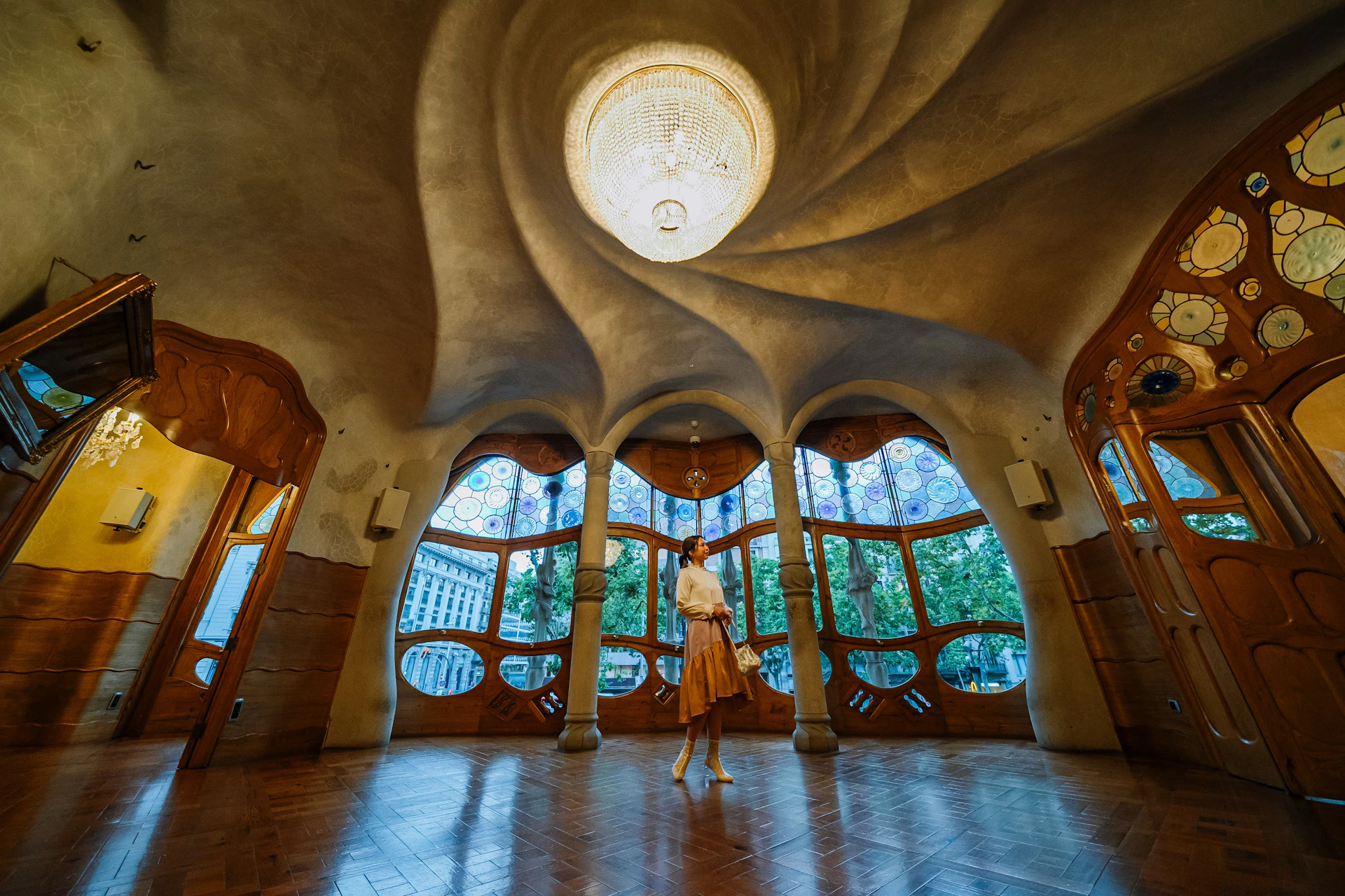 A person stands in an ornately designed room with stained glass windows and a spiral ceiling centerpiece.
