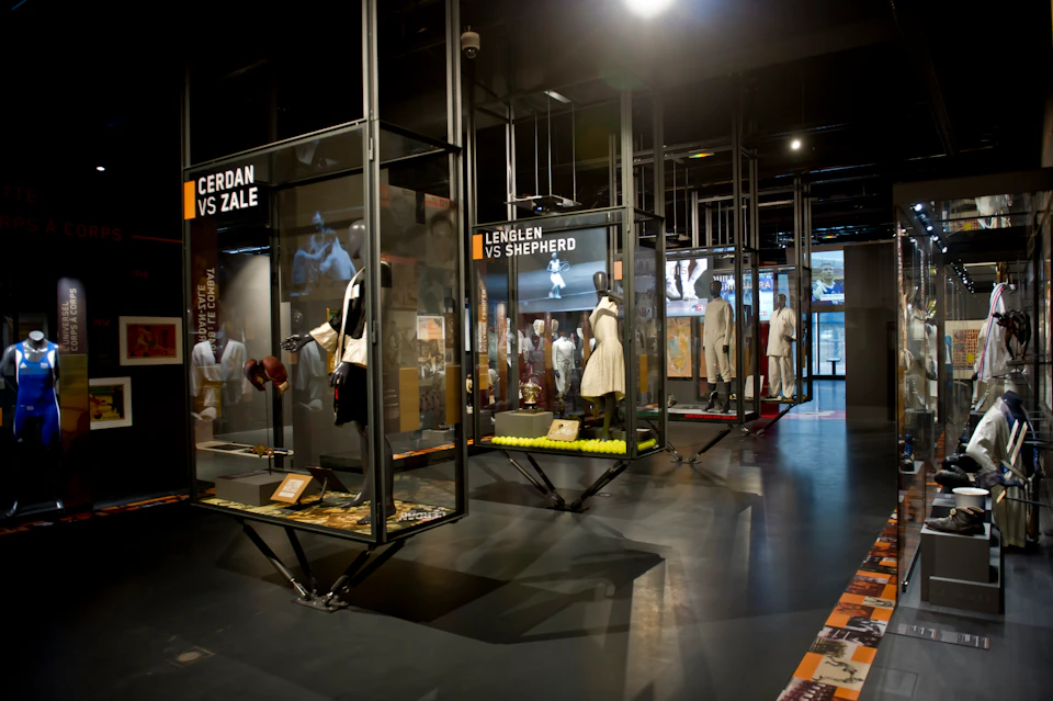 Sports exhibit featuring historic memorabilia and mannequins in glass cases. Signage includes "CERDAN VS ZALE" and "LENGLEN VS SHEPHERD."