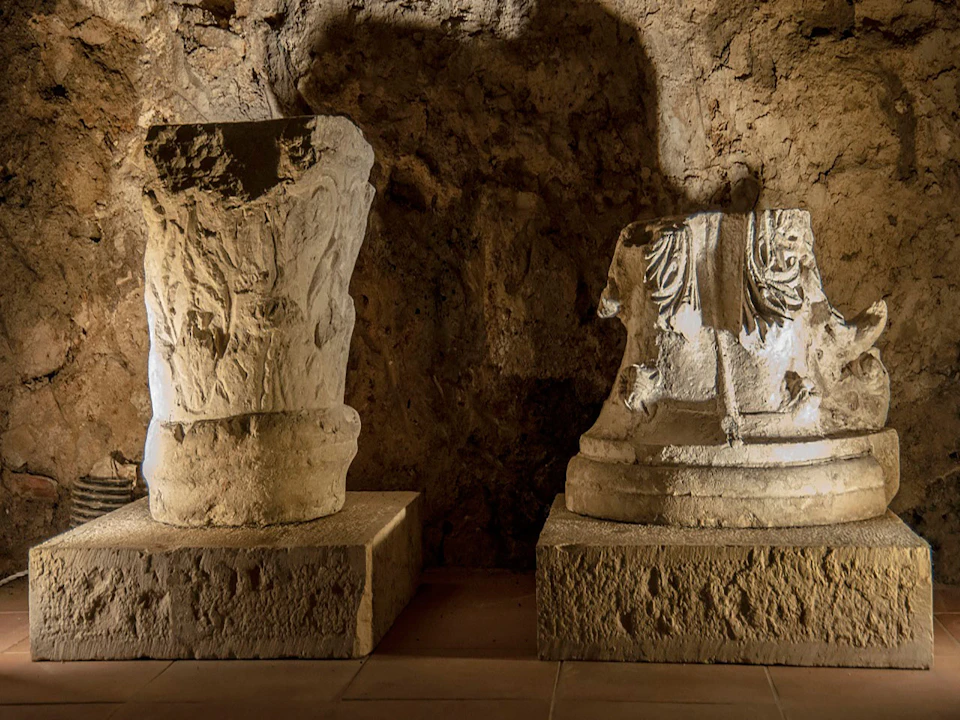 Two ancient, carved stone statues displayed in a dimly lit, rocky cave environment.