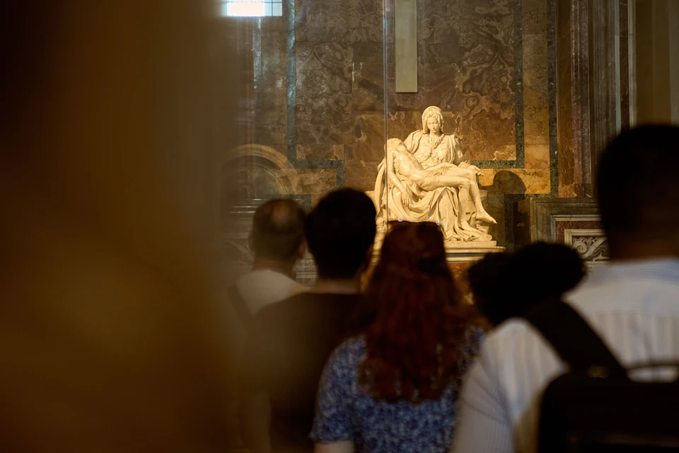 A group of people stand in front of a marble statue in a dimly lit museum or church interior.
