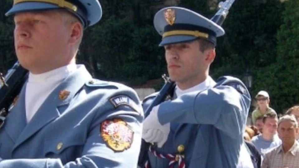 Soldiers in light blue uniforms with swords marching past a crowd in front of a historic building.