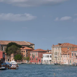 En kanal med färgglada byggnader, båtar dockade och en kyrka i bakgrunden under en blå himmel i Venedig.