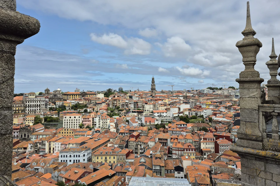 A cityscape with densely packed buildings characterized by terracotta roofs, and a tall tower visible in the background.