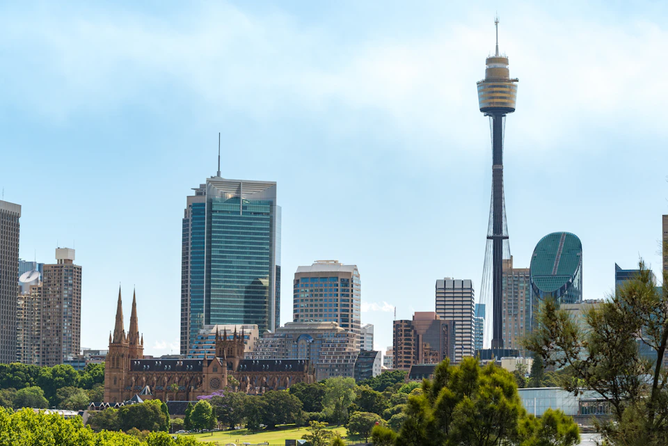 Cityscape featuring Sydney Tower, modern skyscrapers, and the historic St. Mary's Cathedral, with greenery in the foreground.