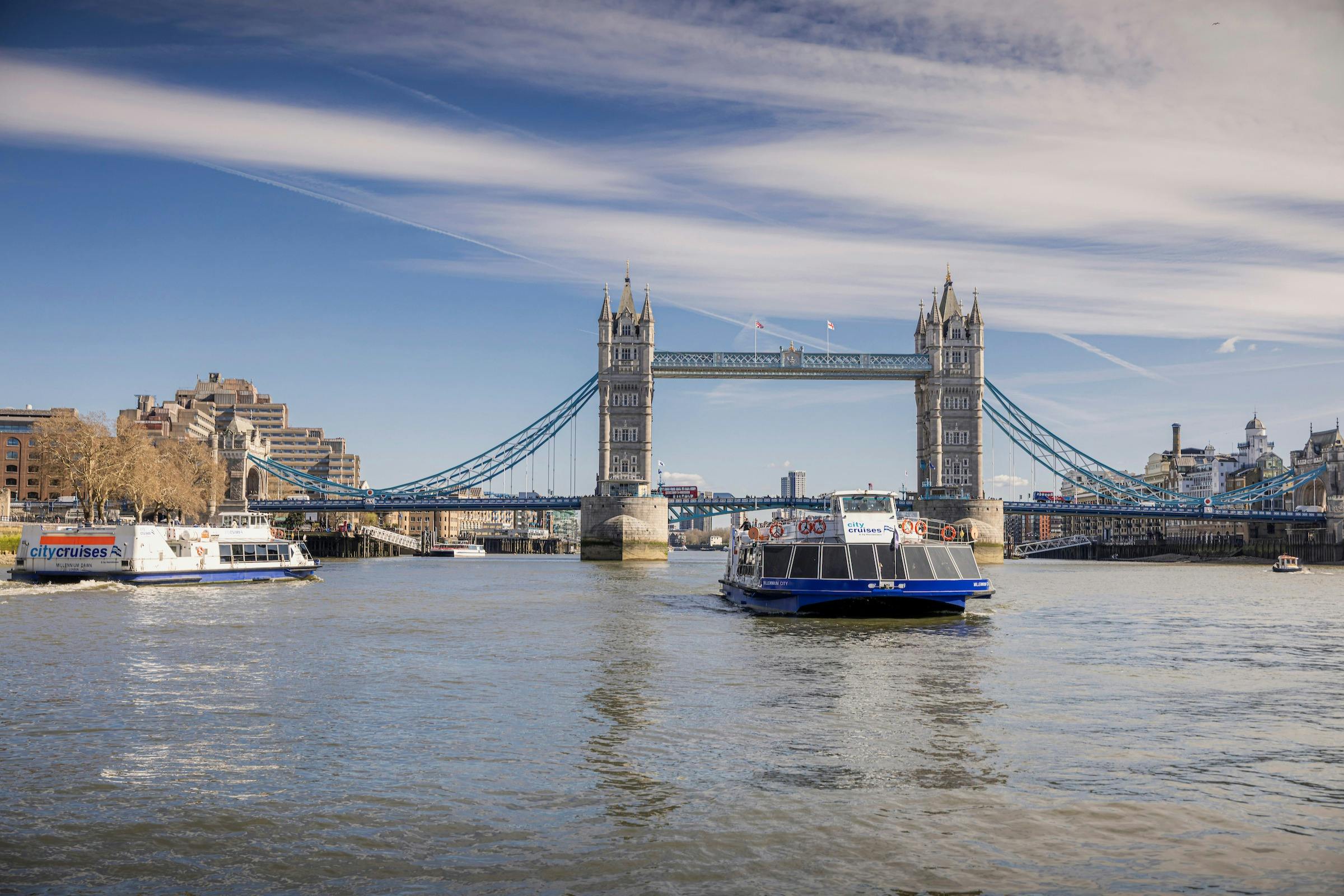 Tower Bridge w Londynie z łodziami na Tamizie pod częściowo zachmurzonym niebem.