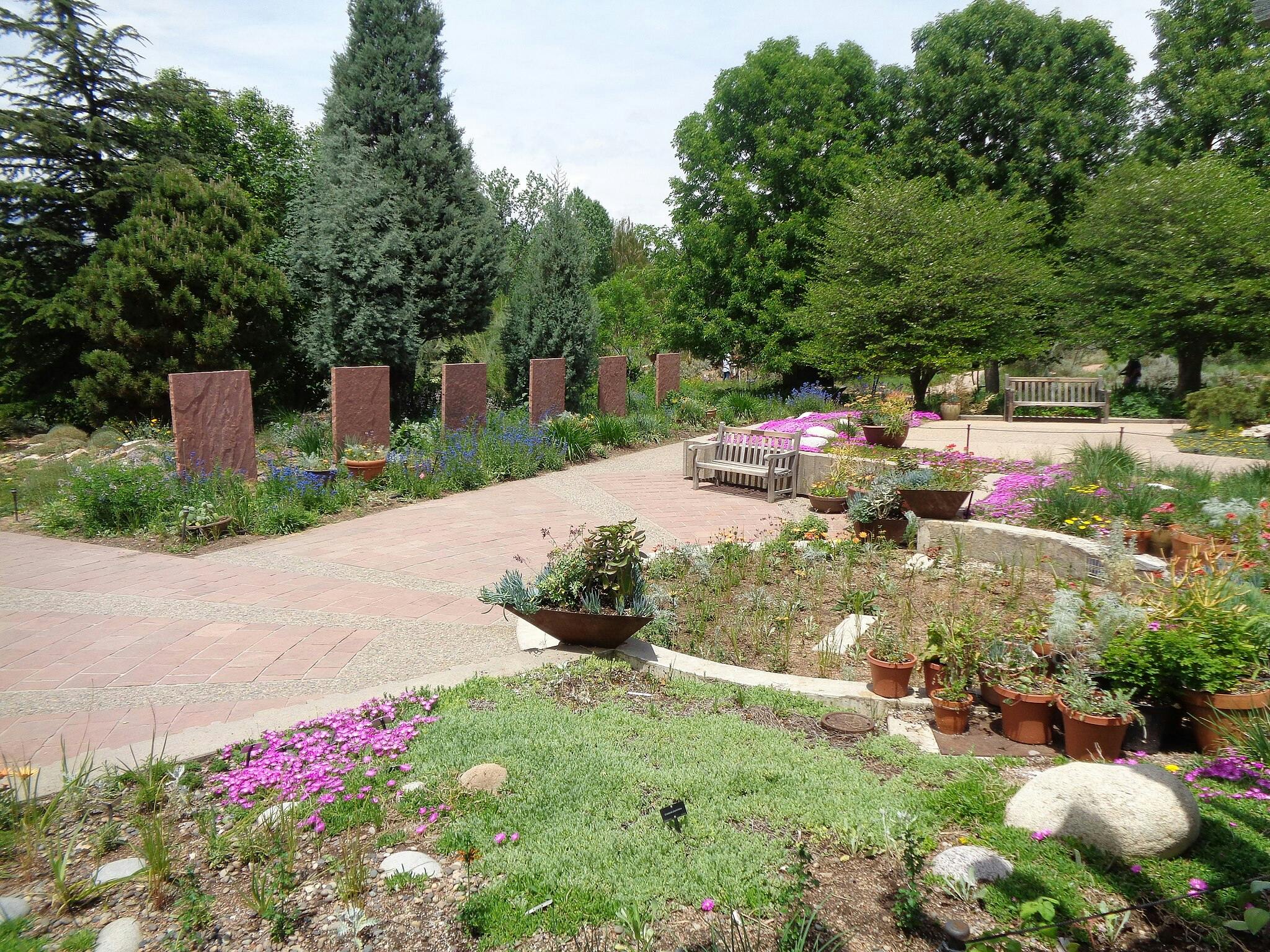 Un giardino paesaggistico con sentieri in pietra, aiuole, panchine, alberi ad alto fusto e lastre di pietra indipendenti sullo sfondo.
