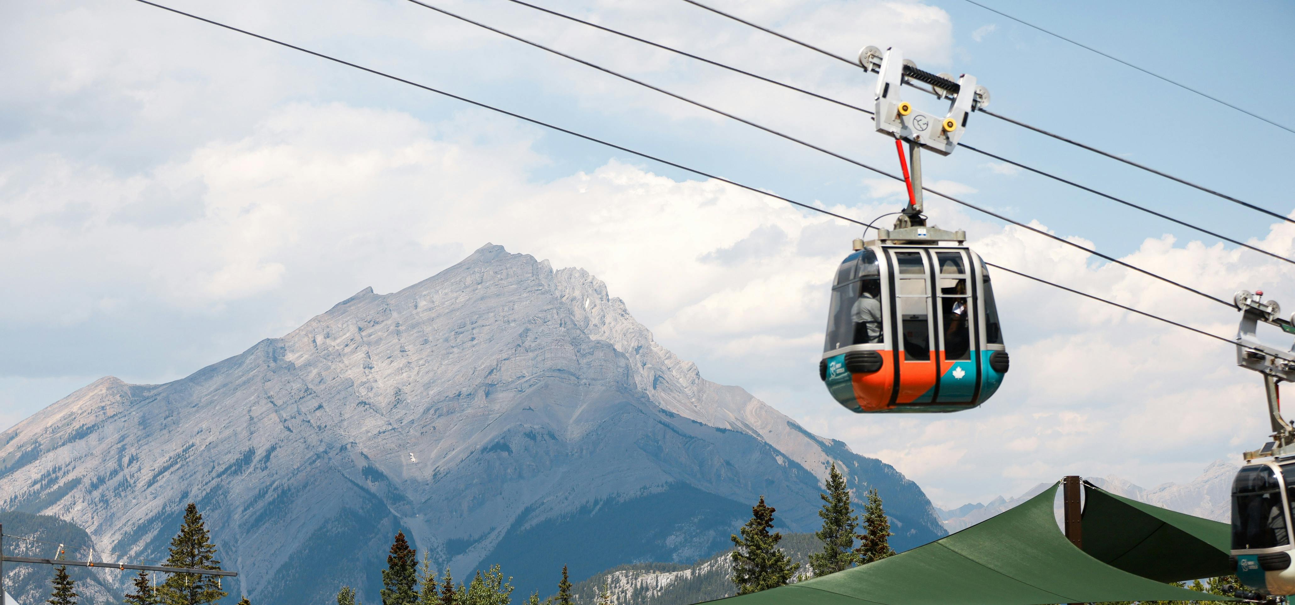 Un telecabina transporta persones per sobre d&#39;una zona boscosa, amb una gran muntanya al fons sota un cel parcialment ennuvolat.