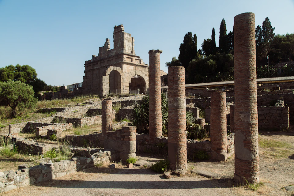 Ancient ruins featuring brick columns and a stone archway against a backdrop of trees and clear sky.