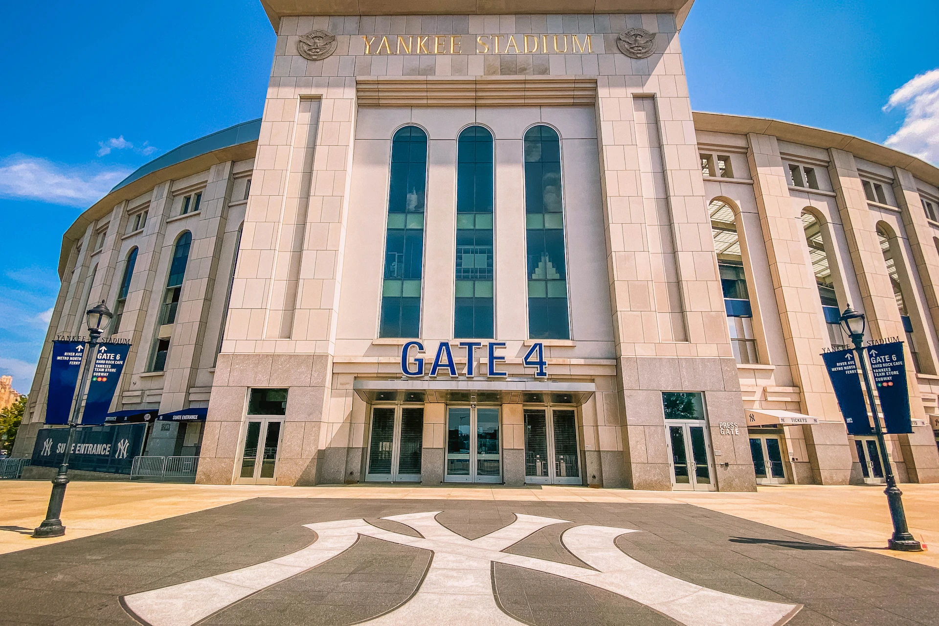 Entrance to Yankee Stadium, showcasing Gate 4 with large glass windows and the iconic Yankees logo on the ground.