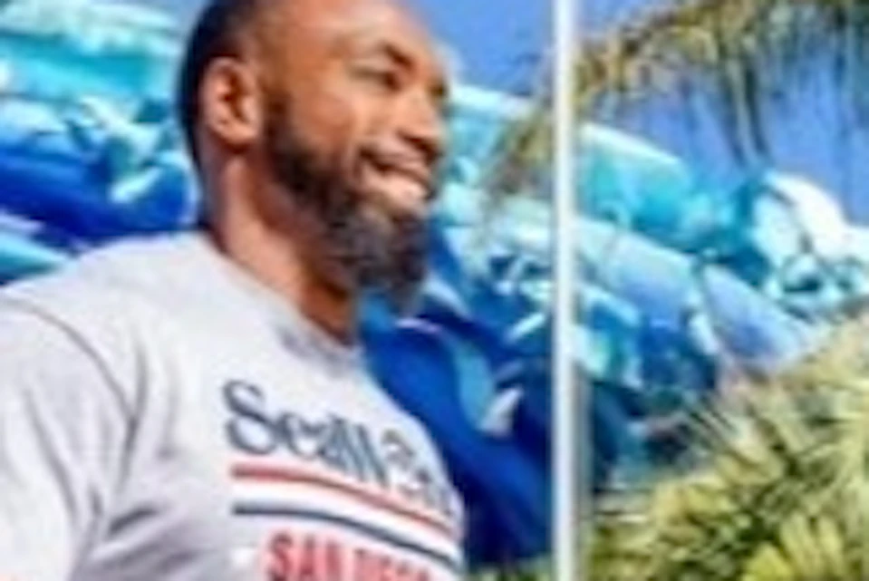 Four people walk together at SeaWorld San Diego entrance, with a large American flag and lush greenery in the background.