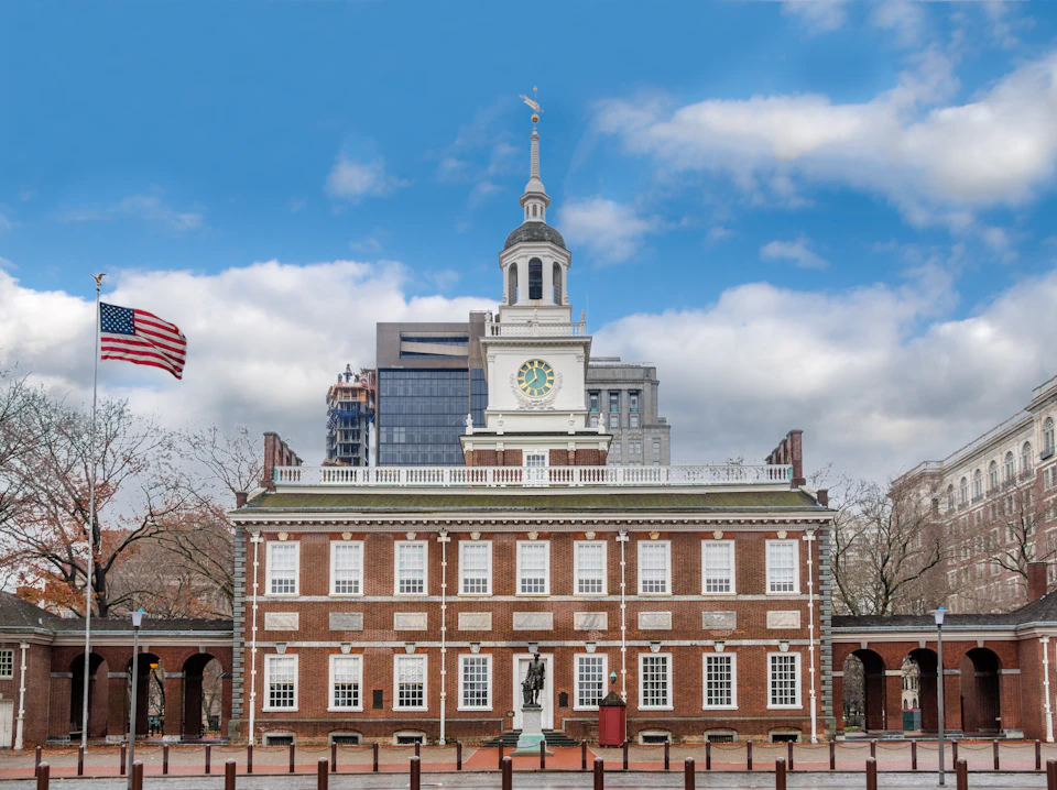 Historic brick building with a clock tower and central statue, an American flag, and a backdrop of modern buildings under a blue sky.