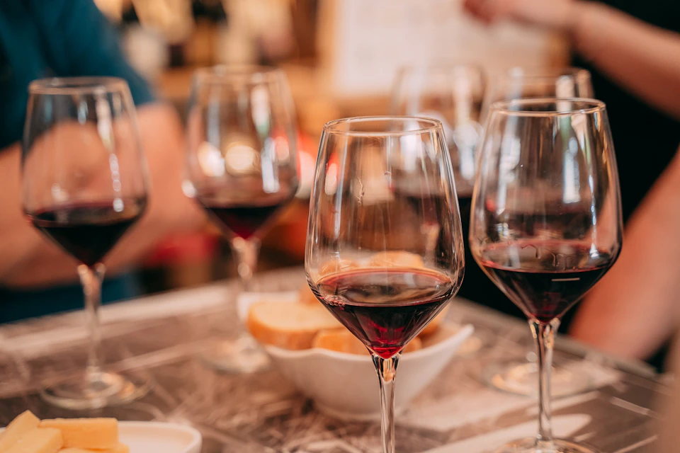 Several glasses of red wine on a table with a bowl of bread in a warm, indoor setting.