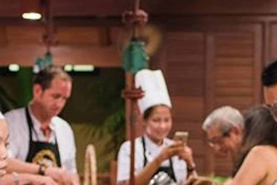 People participating in a cooking class, wearing aprons and chef hats, while using hot plates and kitchen utensils.