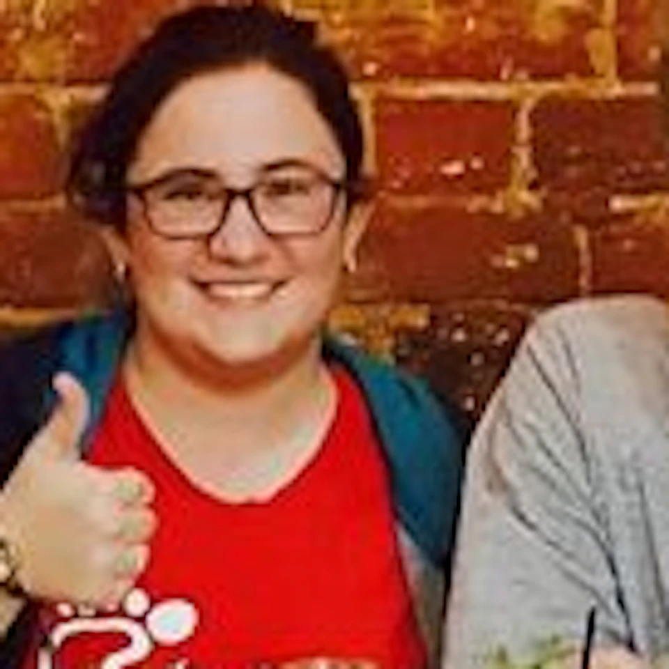 Five people sitting at a wooden table against a brick wall, smiling, with green drinks and condiments on the table.