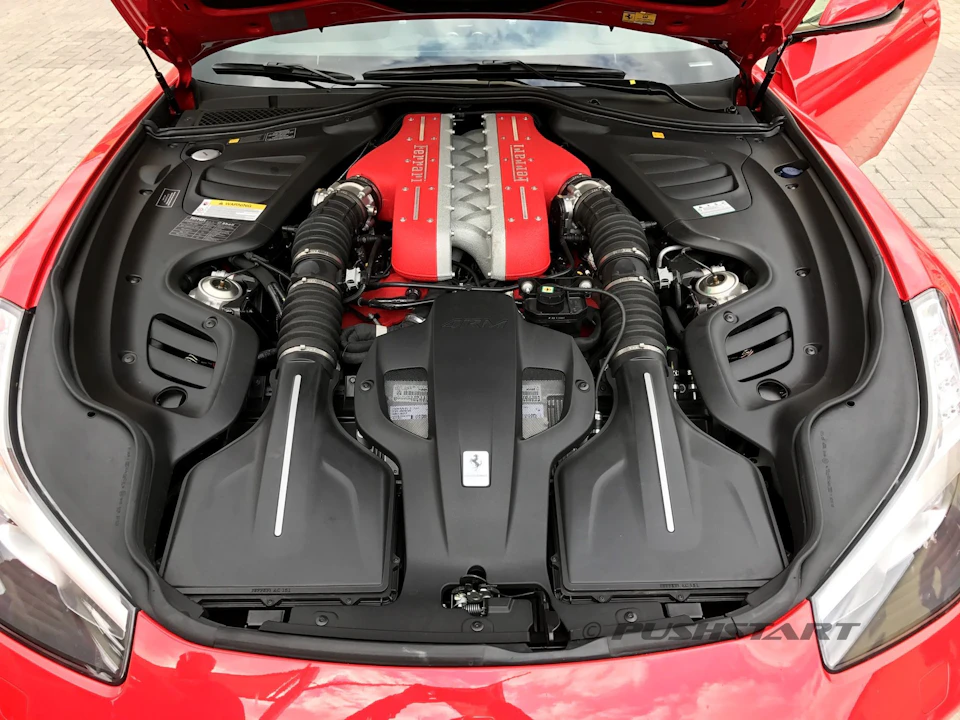 Open hood of a red sports car revealing a red and silver engine with black components and hoses.