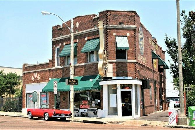 A historic brick building with green awnings and a large guitar sign, featuring a parked red vintage car in front.