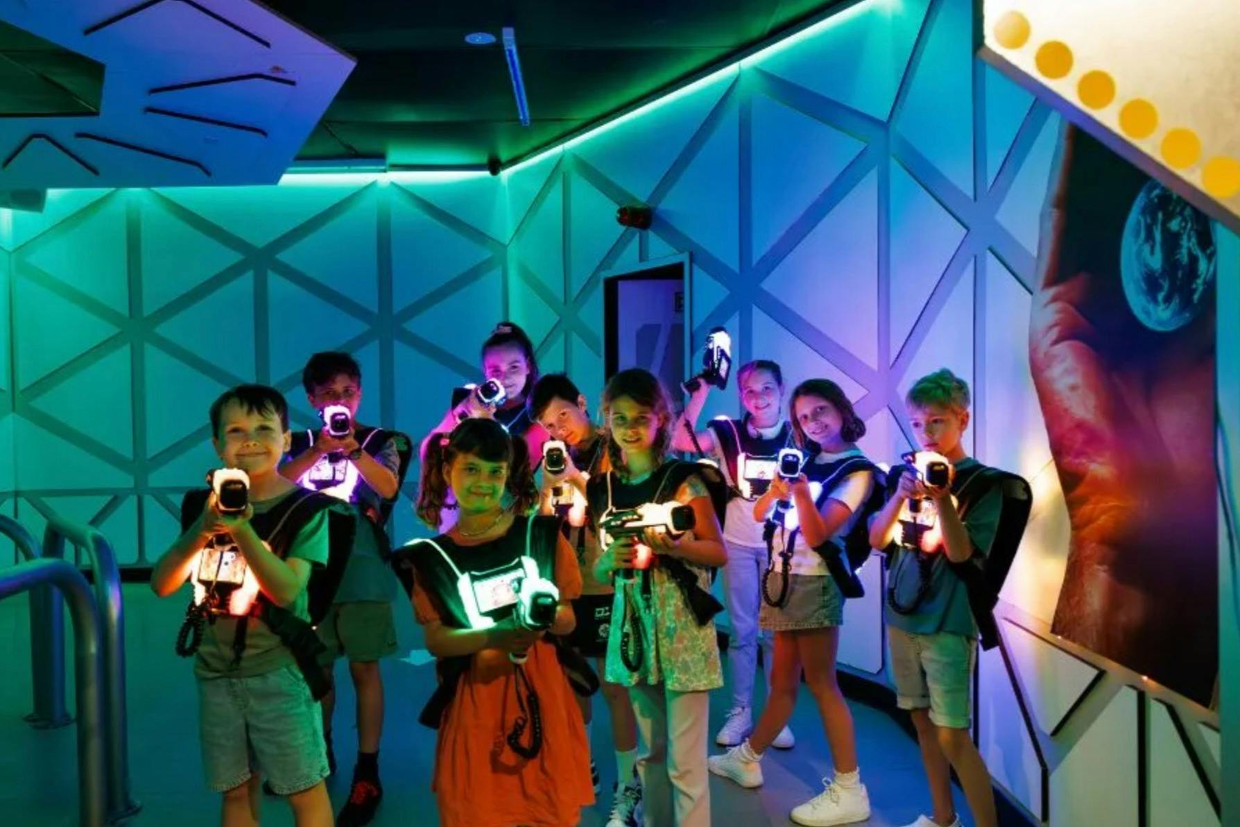 A group of children in a neon-lit space holding laser tag gear, smiling and ready for a game.